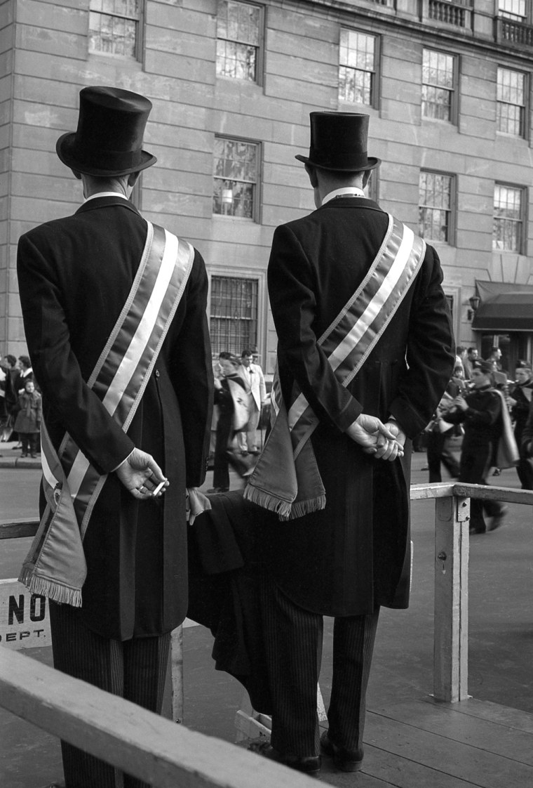Two parade official watch New York's Saint Patrick's Day Parade pass by on Fifth Avenue as one of them sneaks a cigarette break.
